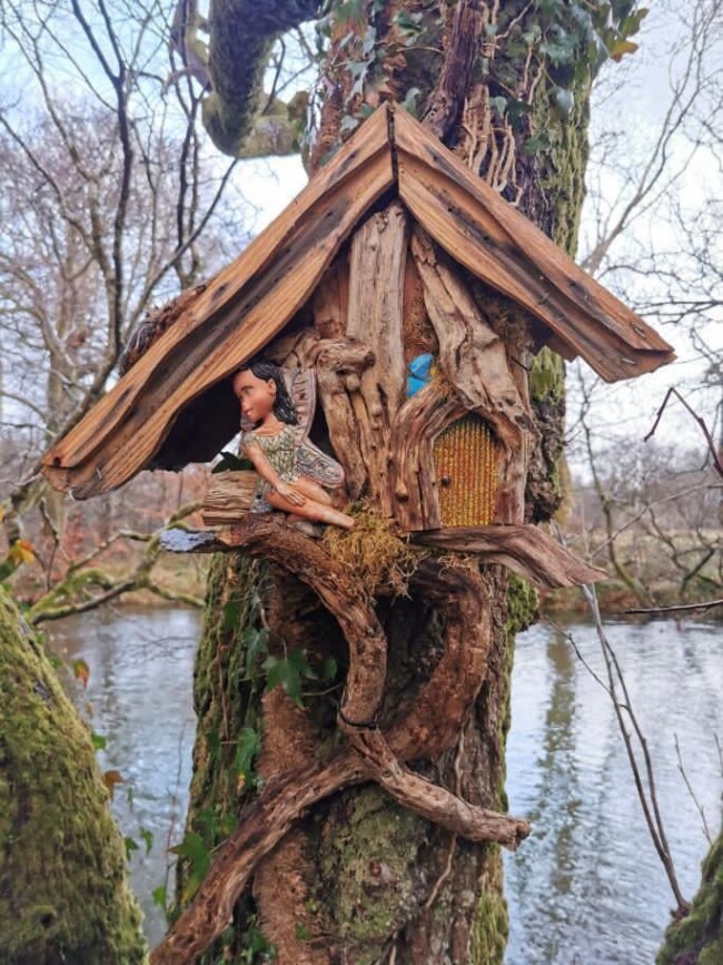 Une maisonnette pour fée, fabriquée avec des morceaux de bois, avec une figurine de fée sculptée.