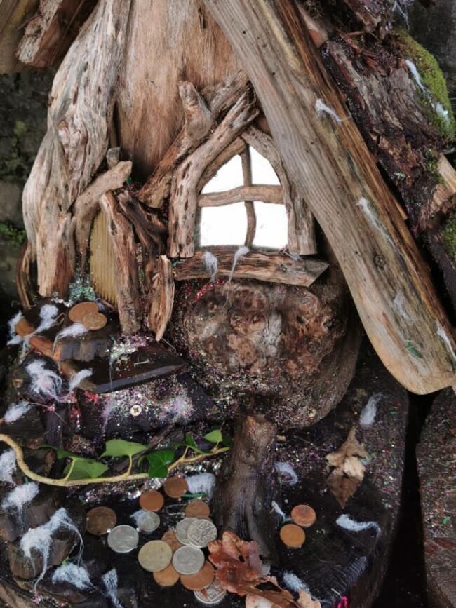 Une maisonnette pour fée en bois, au pied de laquelle ont été déposées des pièces de monnaie.
