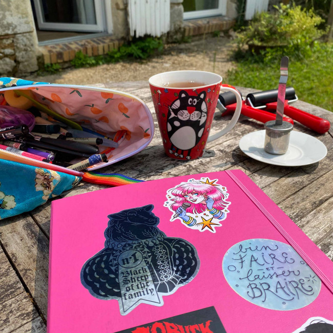 Carnet et matériel créatif sur une table de jardin, dehors.